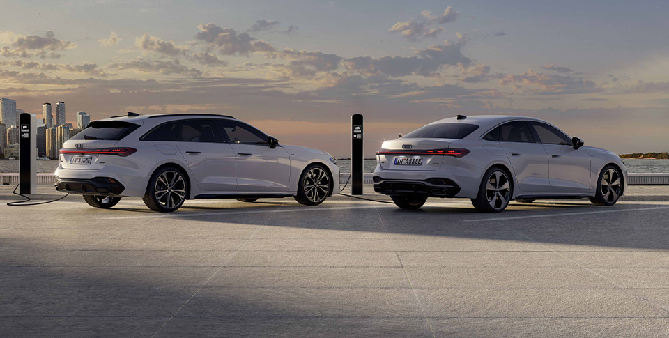 Zwei weiße Audi Elektromodelle an E-Ladesäulen mit Wolken im Hintergrund am Himmel